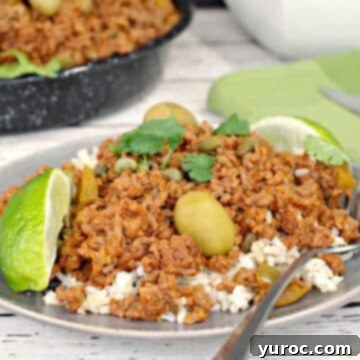healthy picadillo over rice, on a plate with a fork and pan of more picadillo in the background