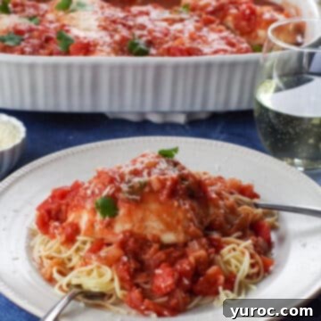 Chicken caccitore on a noodles, on a white plate with a glass of wine and a casserole dish of more chicken caccitore in background