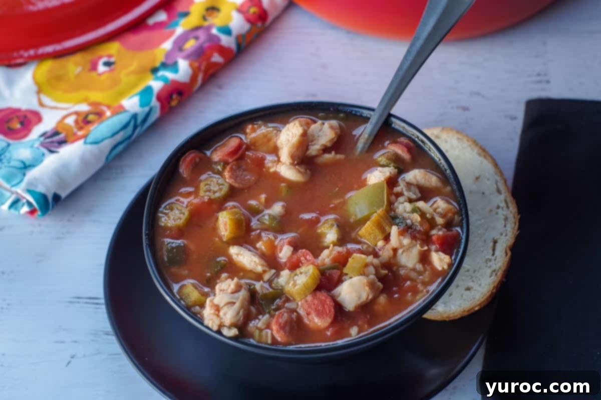 chicken gumbo soup in a black bowl with a piece of buttered rye bread on the side