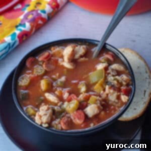 chicken gumbo soup in a black bowl with a piece of buttered rye bread on the side