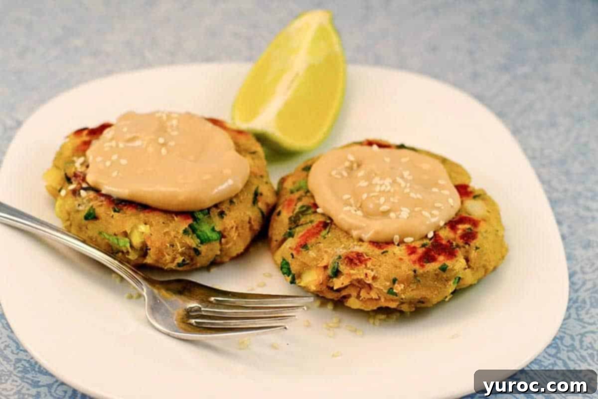 Golden Salmon Cakes with Zesty Ginger Lime Cream 11 2 Pan-fried Salmon Patties on a white plate with creamy sauce on top and a fork and lime wedge on the plate.