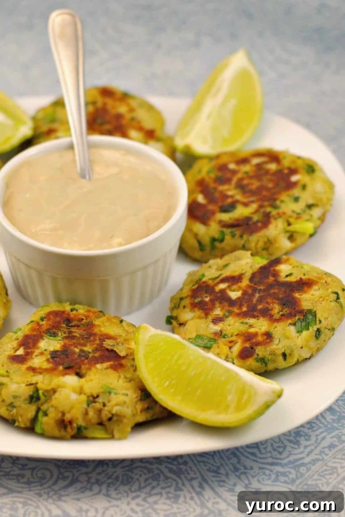 Golden Salmon Cakes with Zesty Ginger Lime Cream 13 Salmon patties on a white plate, with sauce in the middle and lime wedges.