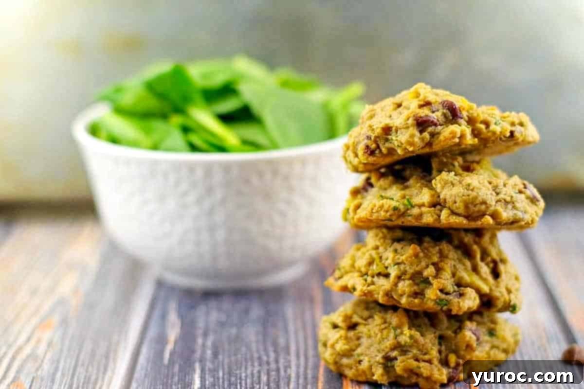 4 healthy chocolate spinach cookies stacked with a bowl of fresh spinach in the background.