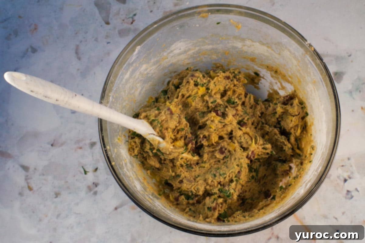 Wet and dry ingredients mixed together in a large glass bowl with a marbled silicone spoon.