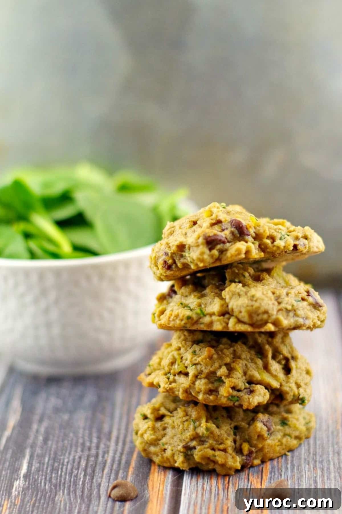 4 healthy chocolate spinach cookies stacked with a bowl of fresh spinach in the background.