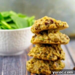 4 healthy chocolate spinach cookies stacked with a bowl of fresh spinach in the background.