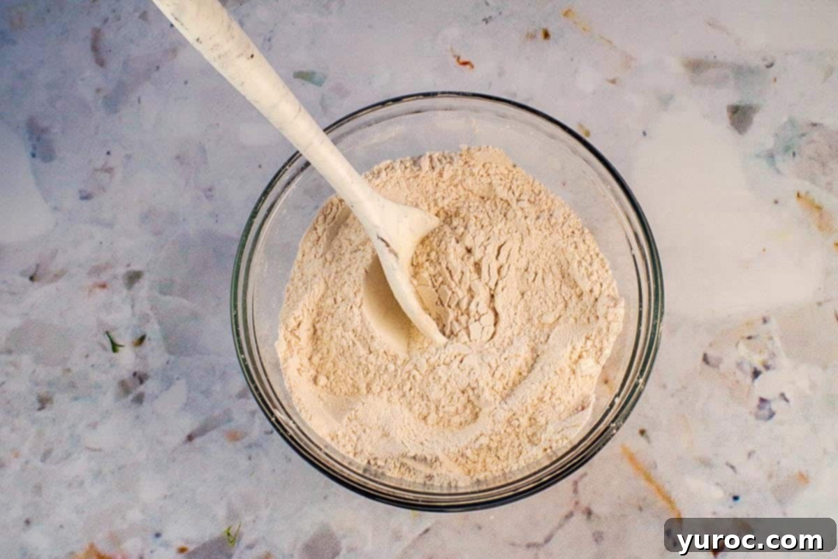 Dry ingredients mixed together in a separate medium glass bowl with a marbled silicone spoon.