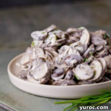 Creamy garlic mushrooms in sour cream, served in a beige bowl on a textured concrete surface, beautifully garnished with fresh springs of green onion.