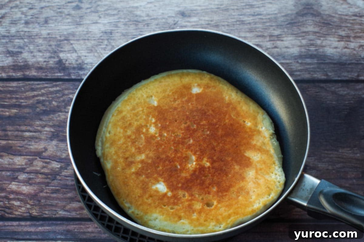 A perfectly golden-brown pancake, just flipped in the frying pan, cooking on its second side.
