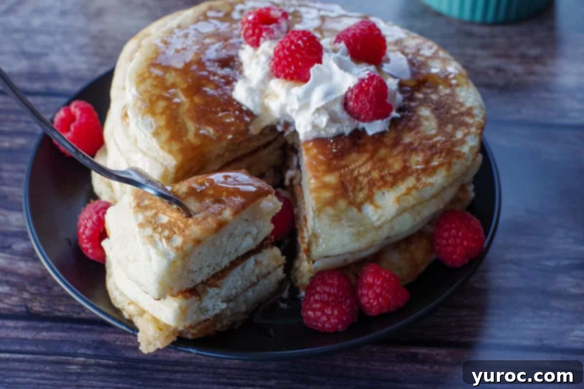 Three fluffy pancakes, stacked and cut, with a fork gently pulling out a piece, revealing the soft, airy interior.