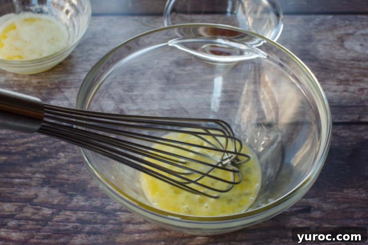 A single egg being vigorously whisked in a separate glass bowl.