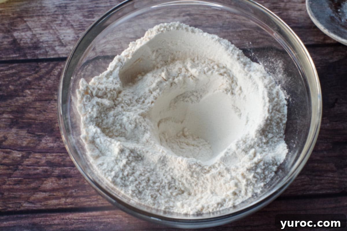 A neatly formed well in the center of the dry ingredients in a glass bowl, ready for liquid additions.