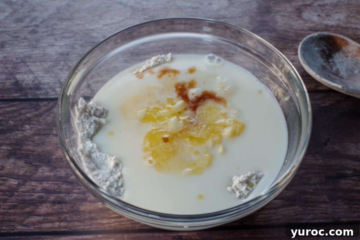 Liquid ingredients, including whisked egg, milk, melted butter, and vanilla extract, being poured into the well of the dry ingredients.