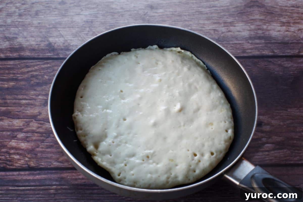 A pancake cooking in a pan, with visible bubbles forming on its surface, indicating it's nearly ready to flip.