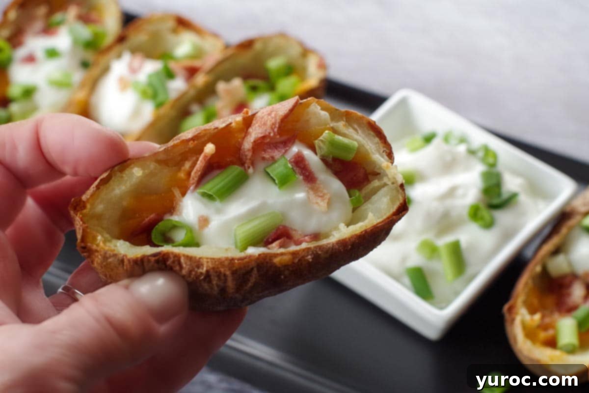 air fryer potato skin being held up over a tray of more air fryer potato skins