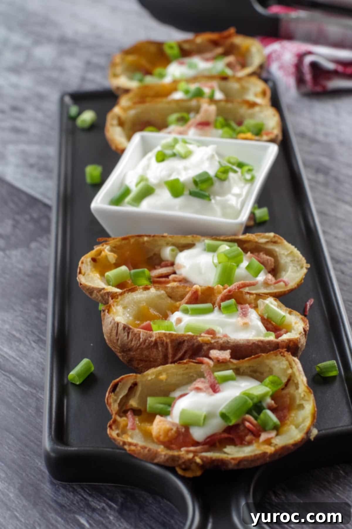 air fryer potato skins on a black platter with a white dish of sour cream in the middle