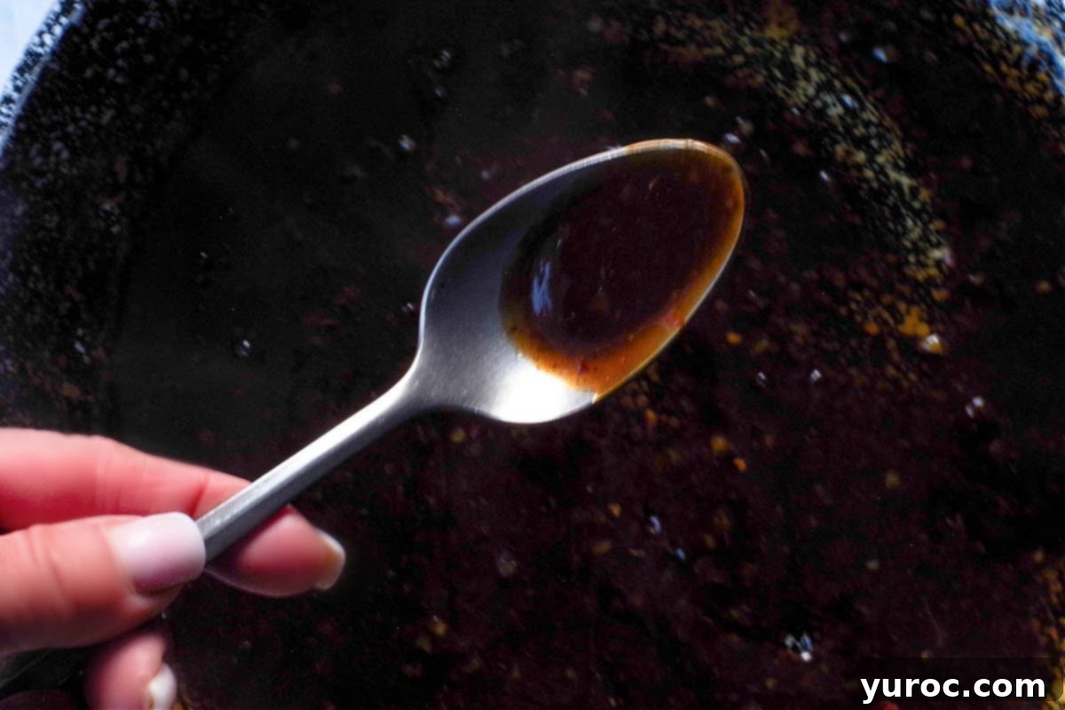 Sticky Orange Hoisin Chicken 10 Thickened hoisin orange sauce being checked with a spoon over the skillet