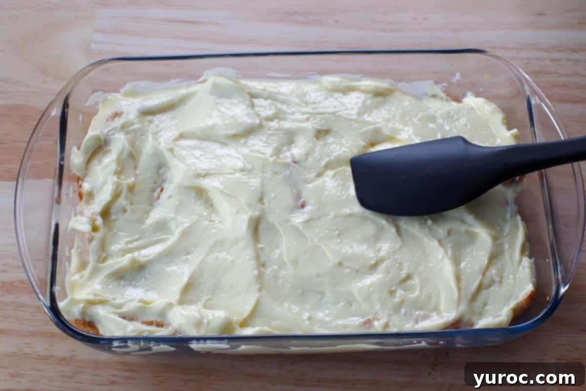 The pudding layer being carefully spread evenly over the croissant base using a black spatula.