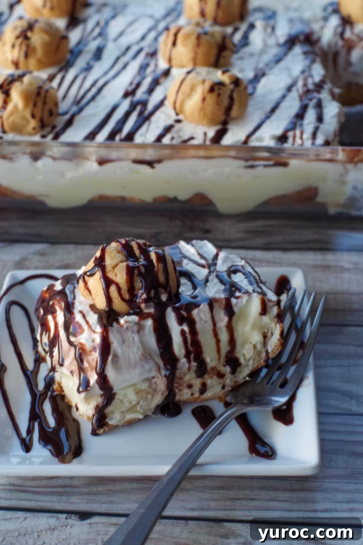 A slice of the No-Bake Cream Puff Dessert on a white plate with a fork, showing the distinct layers. The full pan of dessert is visible in the background.