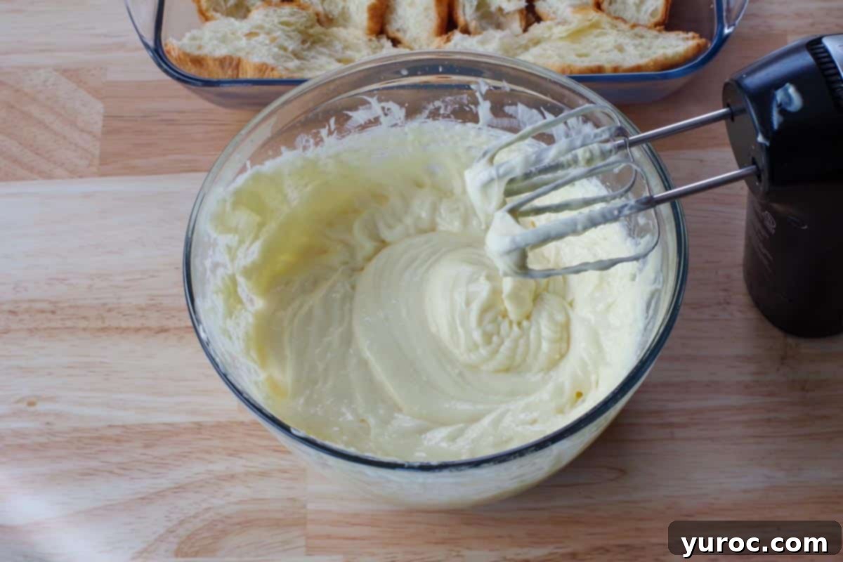 The smooth, combined cream cheese and pudding mixture in a large glass bowl after being thoroughly beaten with an electric mixer.