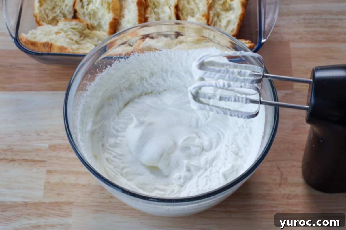 Whipping cream being beaten to soft peaks in a separate bowl, with sugar added during the process.