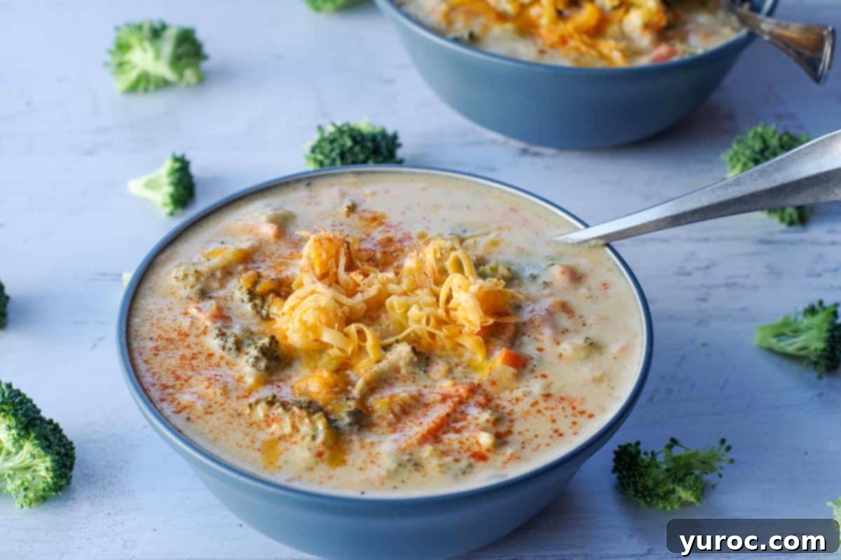 Broccoli cheese soup served in a blue bowl with a spoon, surrounded by fresh broccoli florets