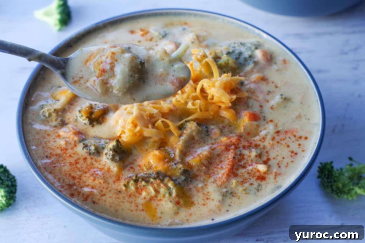 Slow cooker broccoli cheddar soup being held up on a spoon over a bowl