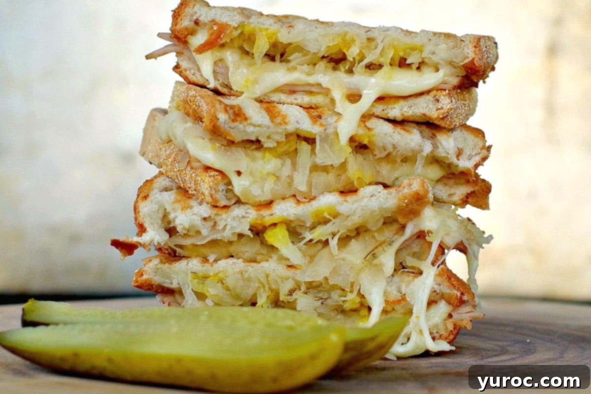 A turkey reuben panini sandwich on a wooden surface with a dill pickle in front.