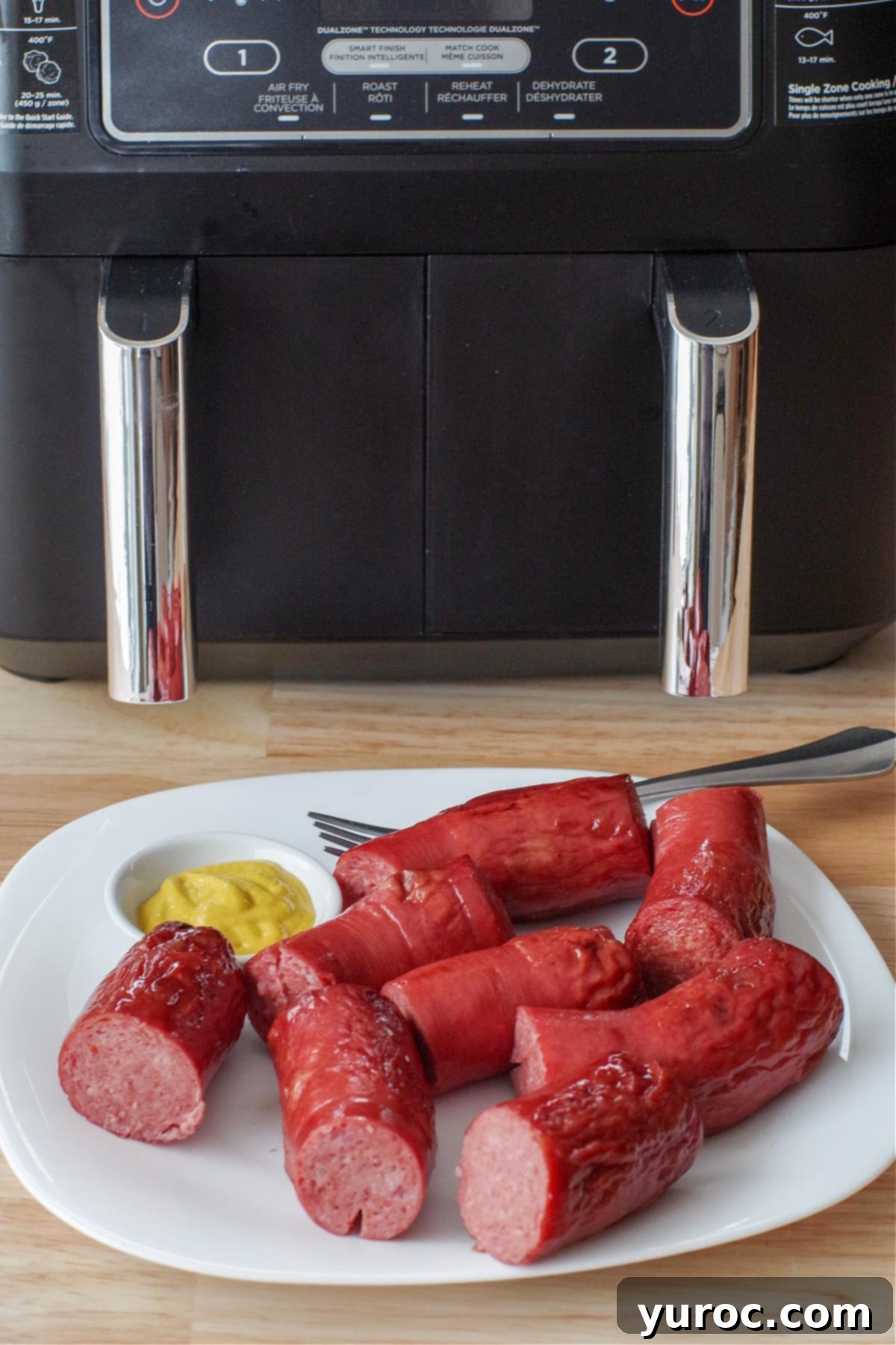kielbasa on a white plate with a small white dish of mustard and tongs, with an air fryer in the background