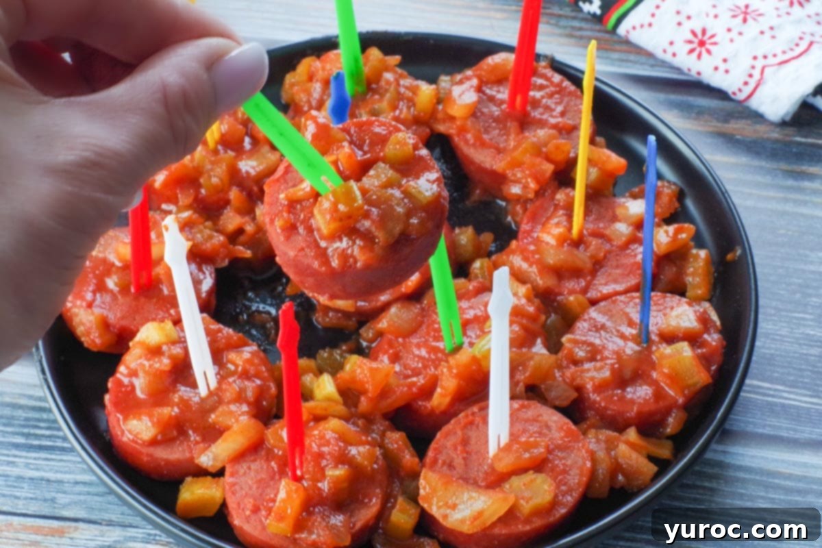 slow cooker kielbasa appetizer on a green plastic skewer being picked up