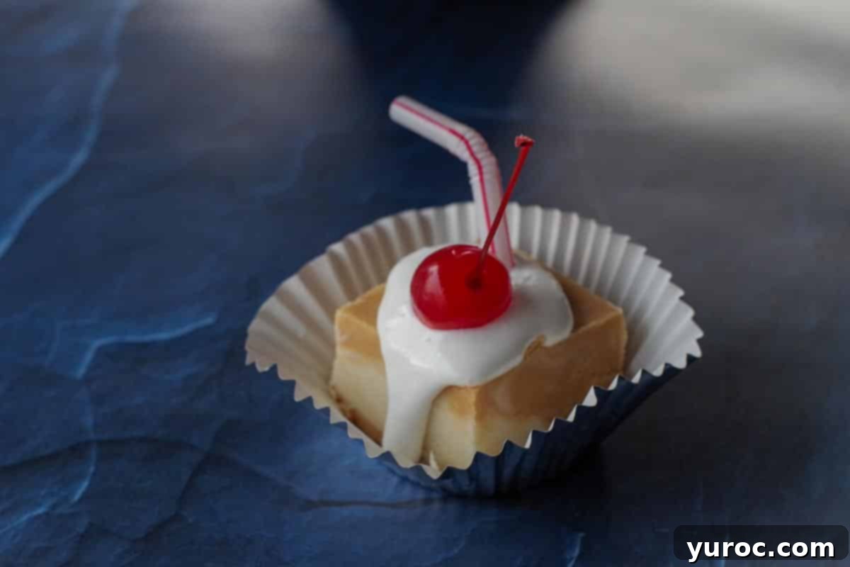 a piece a root beer float fudge on a cupcake liner, with marshmallow fluff and cherry, with a straw in it on a blue surface