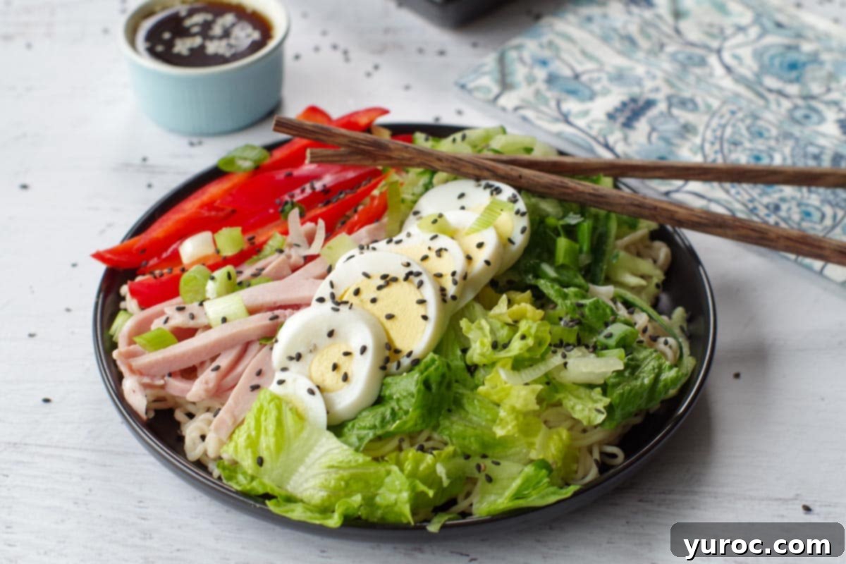Japanese cold noodle salad on a black plate, with chopsticks and a dish of dressing in the background