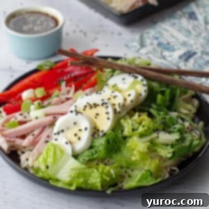 Japanese cold noodle salad on a black plate, with chopsticks and a dish of dressing in the background