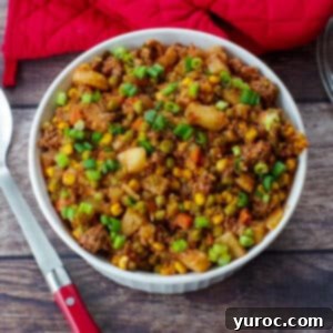 shipwreck casserole on a wooden surface with red oven mitts in background and spoon to the right.