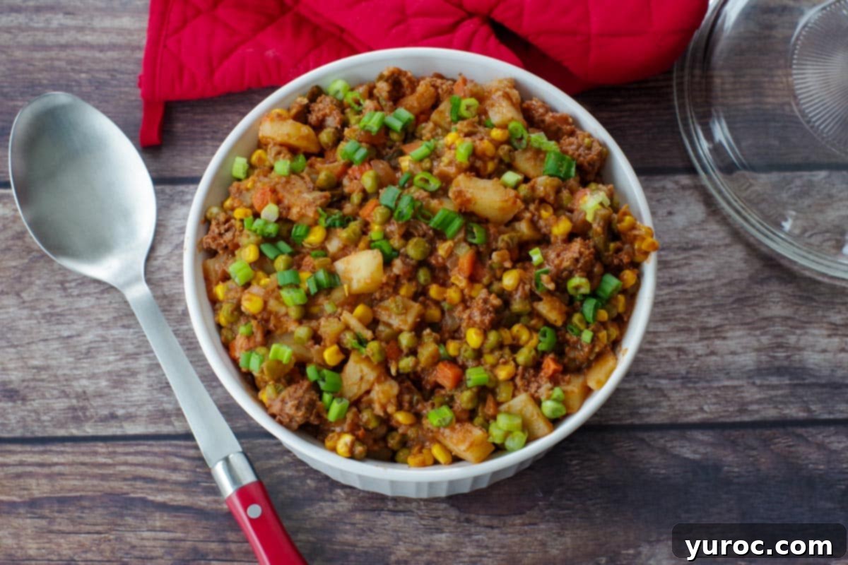 shipwreck casserole on a wooden surface with red oven mitts in background and spoon to the right.
