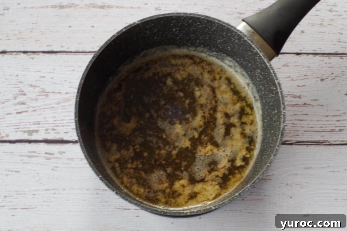 Brown butter being carefully added to the honey and milk mixture in a saucepan.