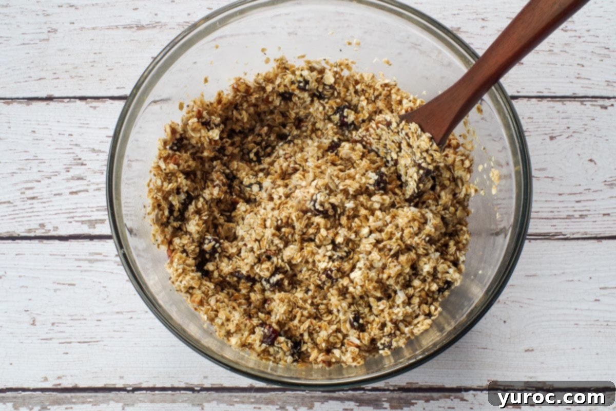 Liquid ingredients being poured over the dry oat mixture in a large glass bowl.