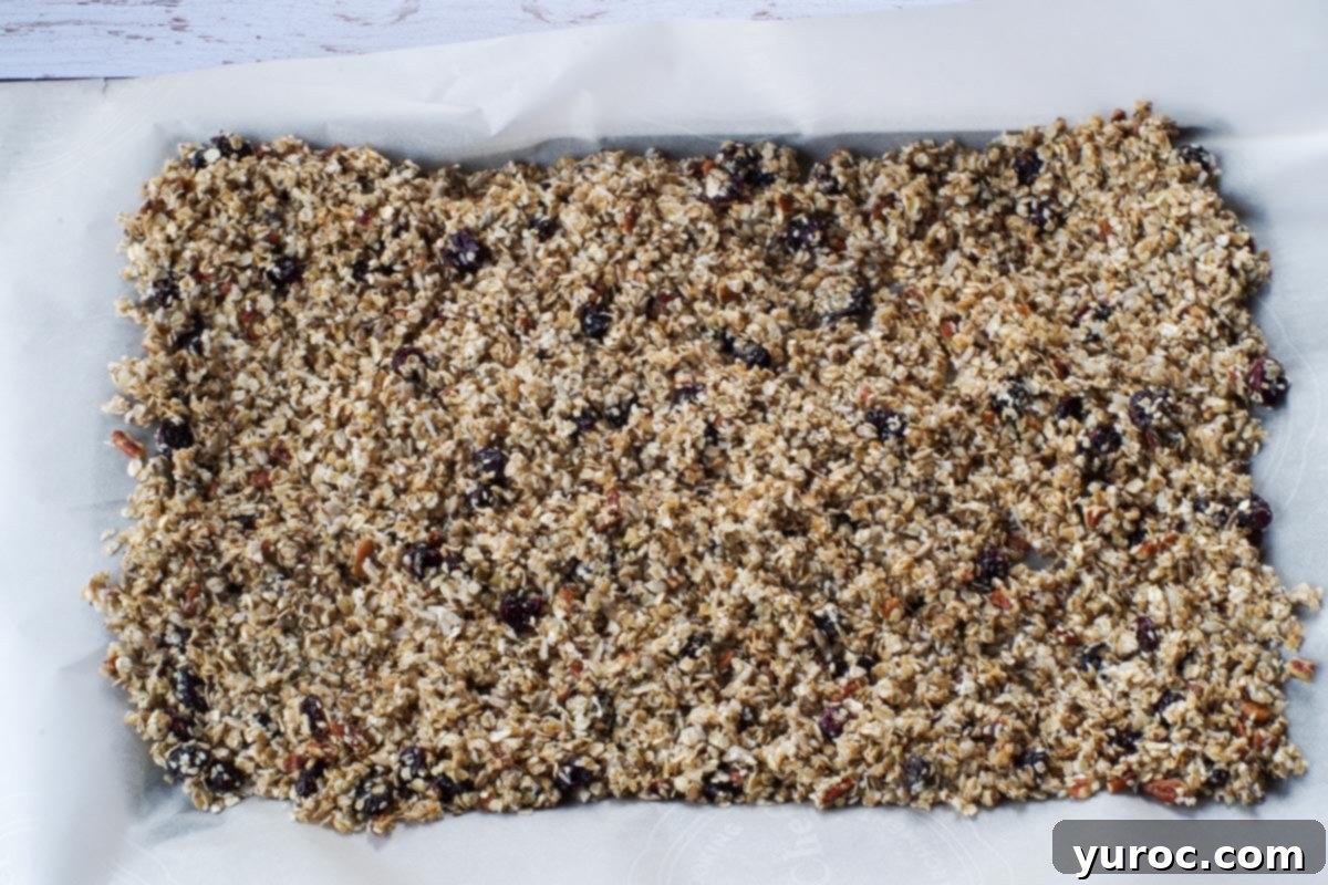 Granola mixture spread evenly on a parchment-lined baking sheet, ready for the oven.