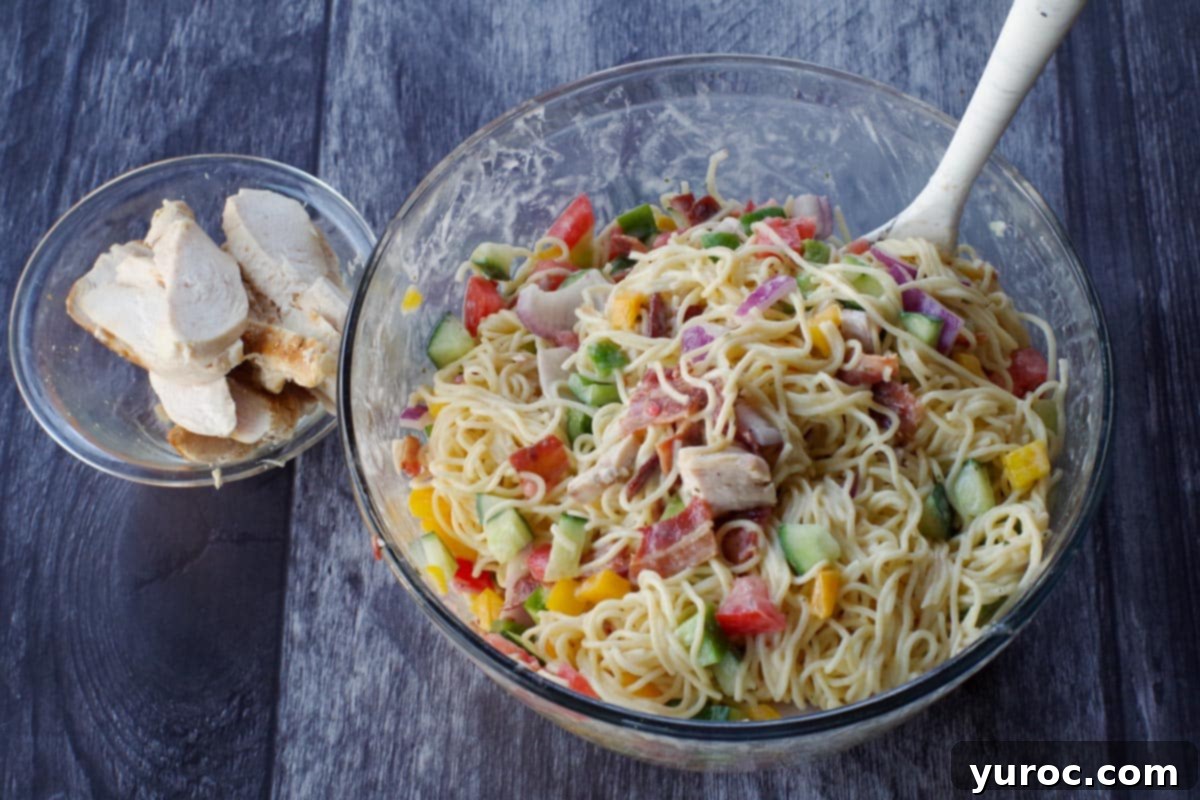 Ultimate Creamy Bacon Ranch Chicken Pasta Salad 4 salad ingredients mixed together in large glass bowl with chicken in small glass bowl, on the side