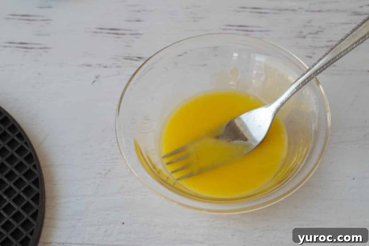 Two egg yolks lightly beaten with a fork in a small glass bowl.