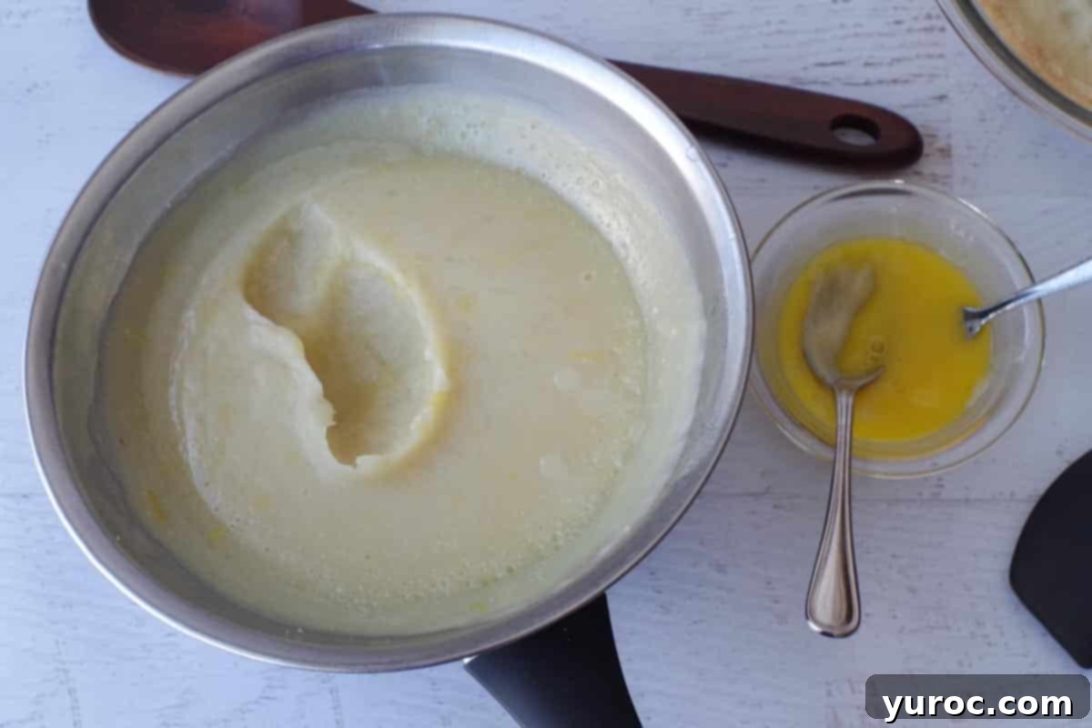 A small amount of hot lemon mixture being carefully added to the beaten egg yolks.