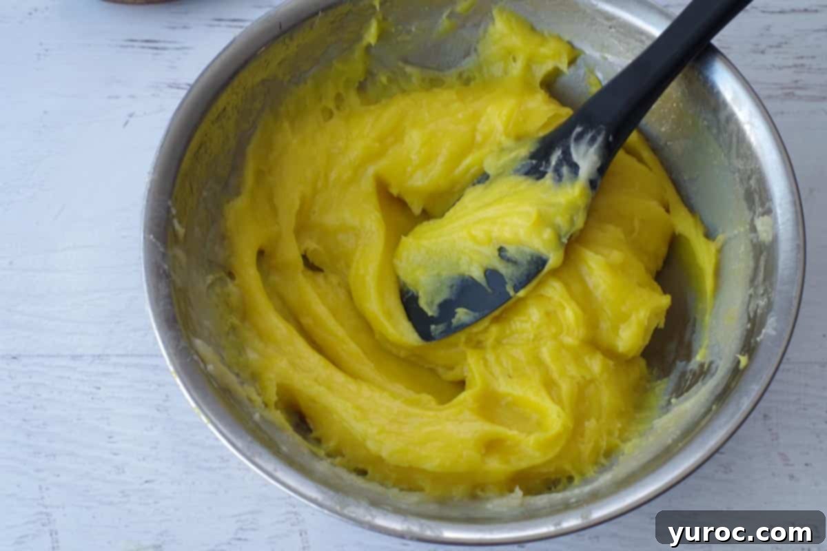 Yellow food coloring being mixed into the lemon pie filling in a stainless steel bowl.