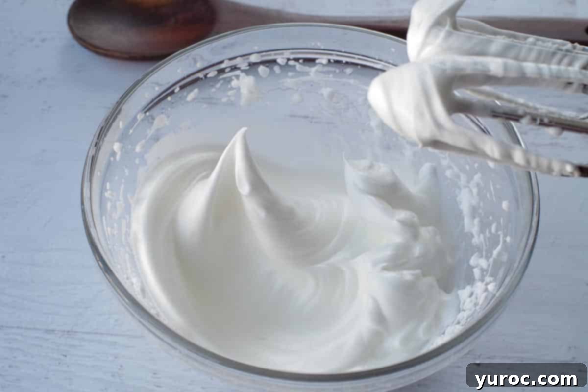 Sugar being gradually added to beaten egg whites and mixed until the meringue holds its shape.