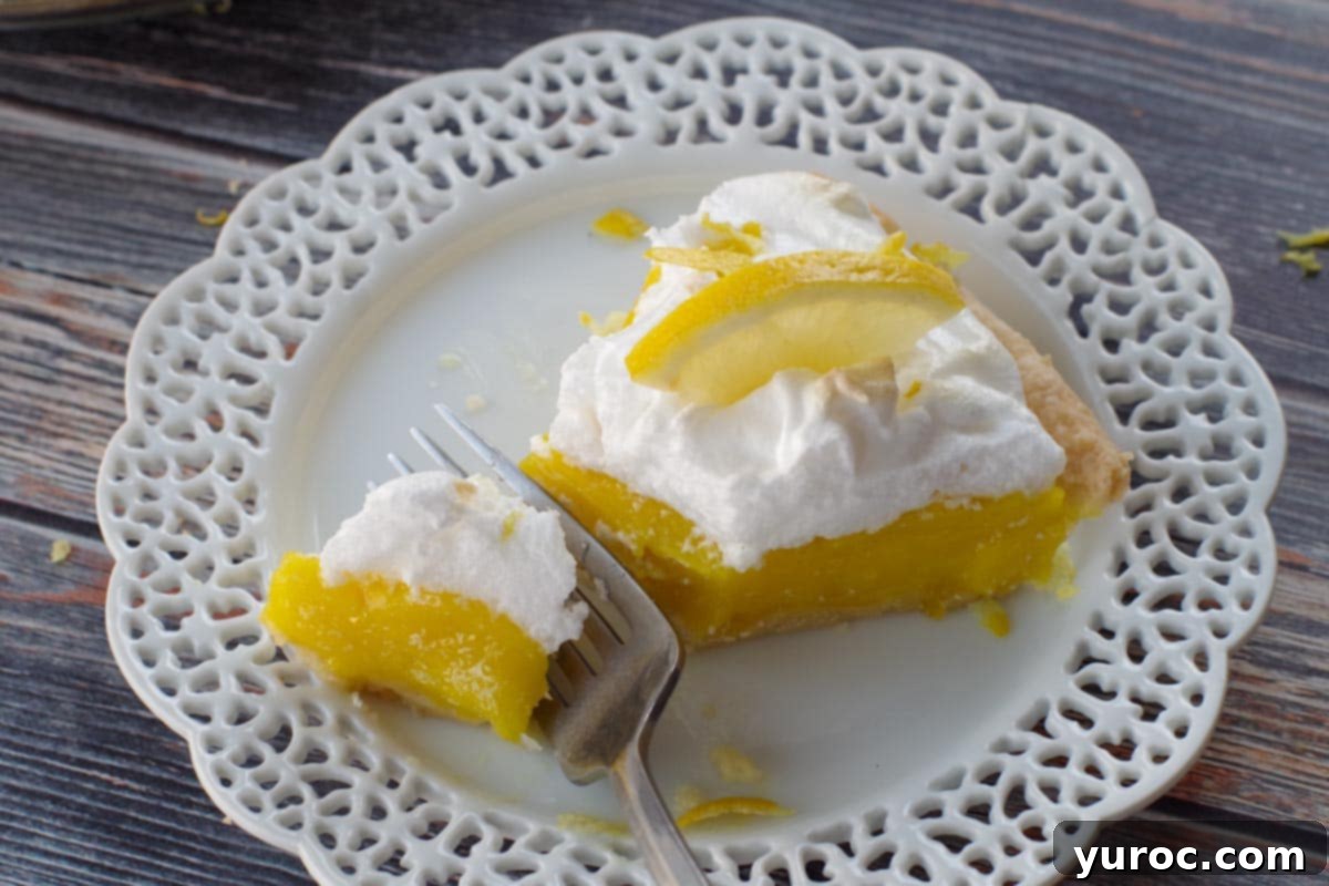 A slice of old-fashioned lemon pie being cut into with a fork on a white plate with decorative lattice edges, highlighting its creamy texture.