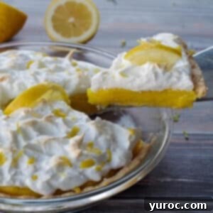 A piece of homemade lemon meringue pie being lifted out of a whole pie, with a lemon cut in half in the background, ready to be enjoyed.