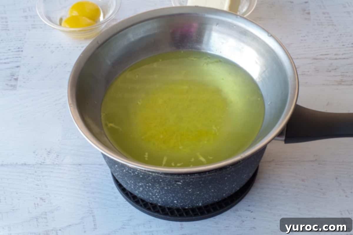 Lemon zest simmering with water in a makeshift double boiler on a stovetop.