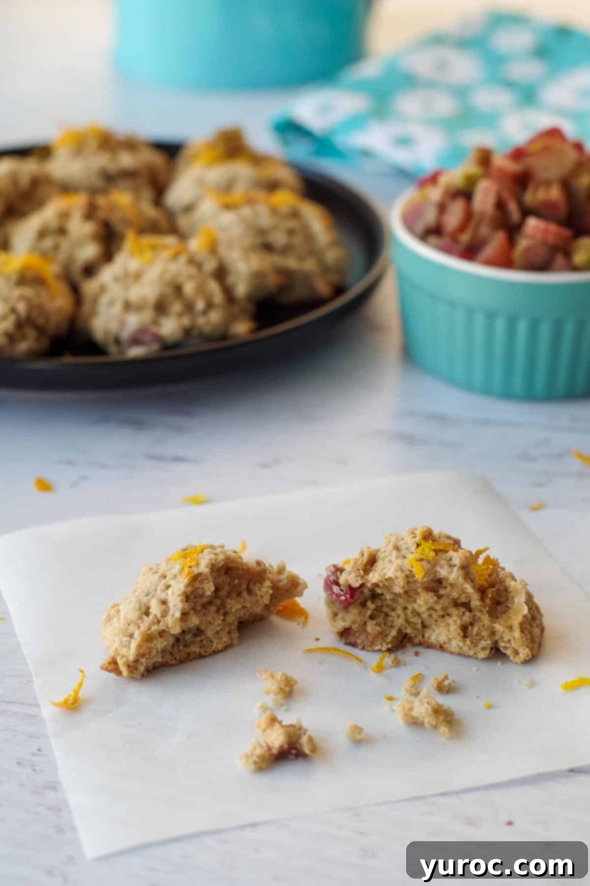 Sweet & Tart Rhubarb Oat Cookies 2 A perfectly baked rhubarb oatmeal cookie, broken in half, resting on a piece of parchment paper, revealing its soft, chewy interior and pink rhubarb pieces.