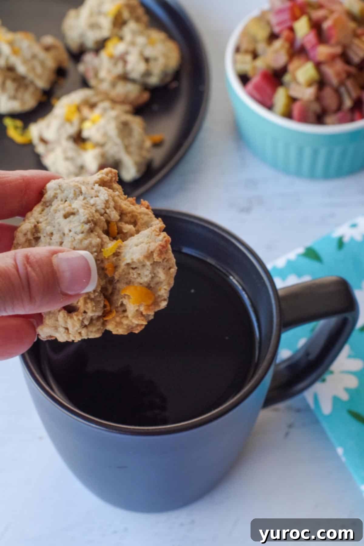 Sweet & Tart Rhubarb Oat Cookies 16 A golden-brown rhubarb oatmeal cookie being gently dipped into a black ceramic mug filled with steaming coffee, suggesting a perfect pairing.