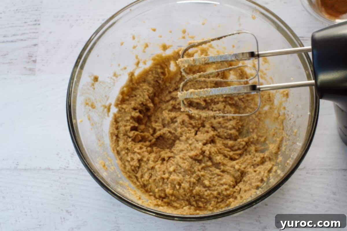 Sweet & Tart Rhubarb Oat Cookies 6 An electric mixer with beaters is shown actively mixing the butter, sugars, egg, and vanilla extract in a glass bowl until the mixture is light and fluffy.