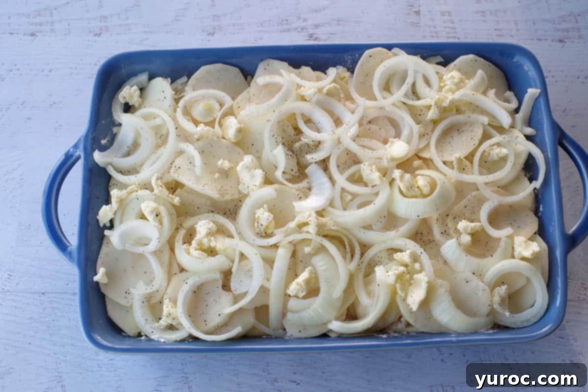 final layer of potatoes, onions, butter and salt and pepper with milk poured over top, in a blue casserole dish